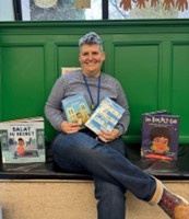 Seated person holding up children's books and smiling
