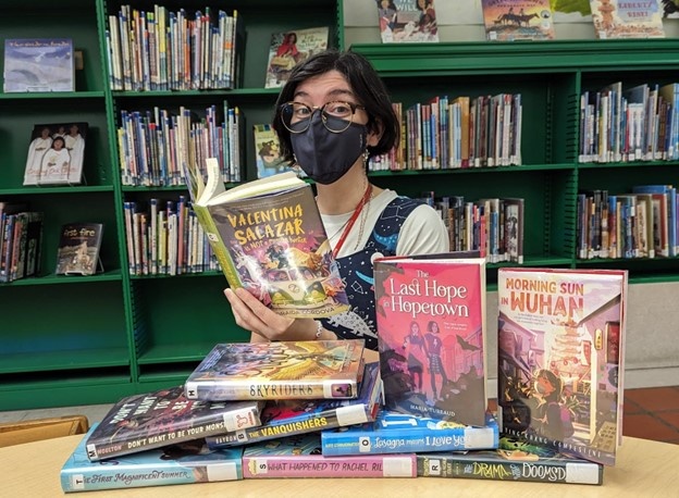 Person holding up a children's picture book in front of bookshelves