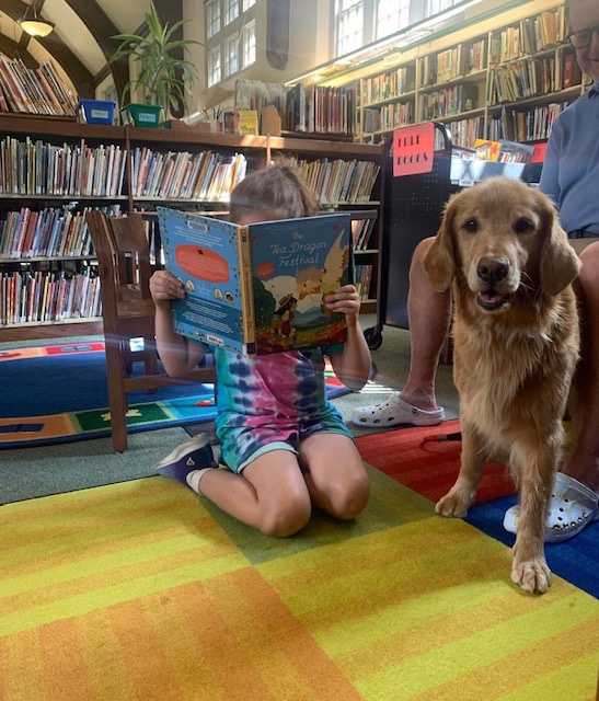 A doggy visitor from PAWS enjoys a storytime from a young reader.