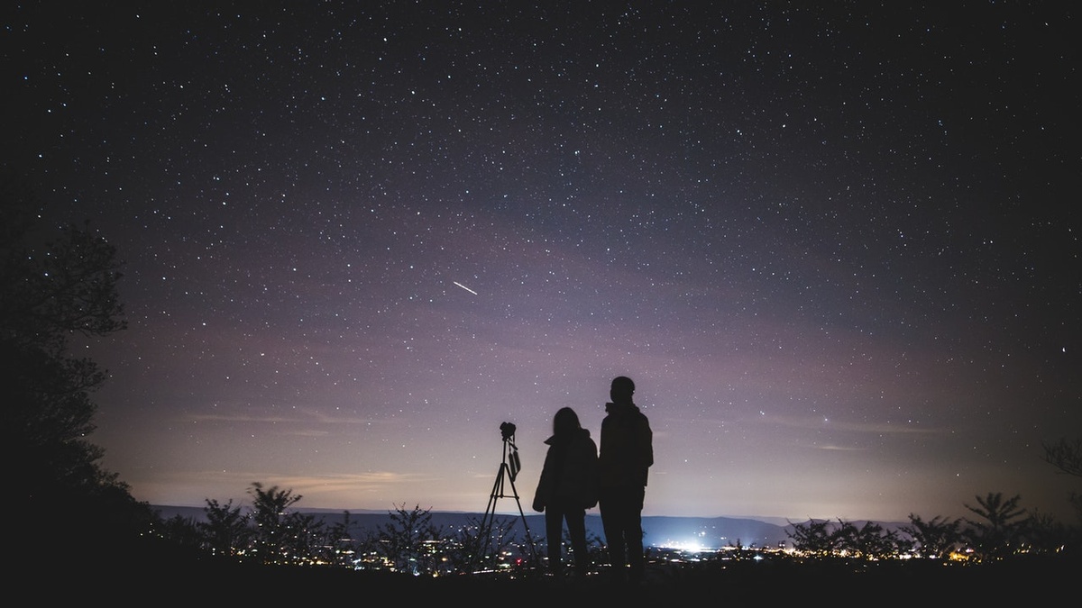 A parent and child stand before a telescope, admiring the night sky.