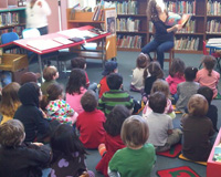 Elizabeth Corbett, Children's Librarian at the Charles Santore Branch Library, shares a book with some young readers.