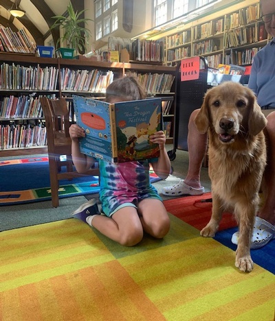 A doggy visitor from PAWS enjoys a storytime from a young reader.