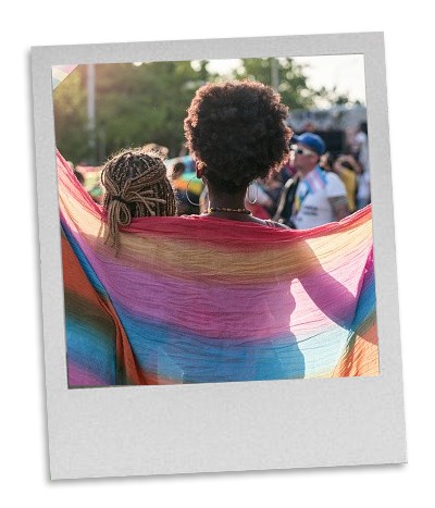 a Polaroid style photo picturing two figures draped beneath a rainbow shawl